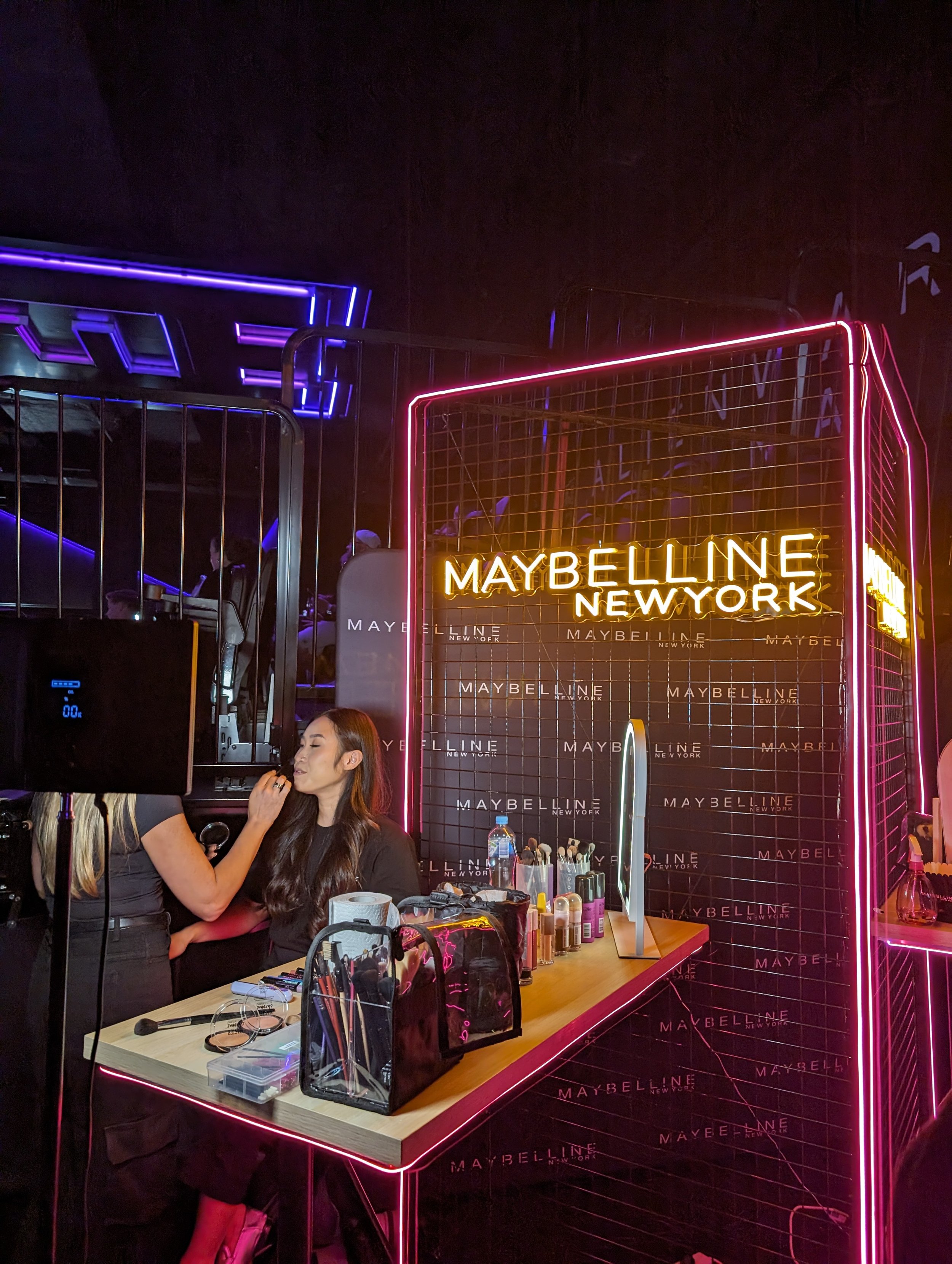 Someone getting their makeup done in front of a neon sign