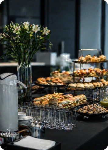 Mesa de catering executivo com finger foods refinados e decoração elegante para recepção empresarial de alto padrão.