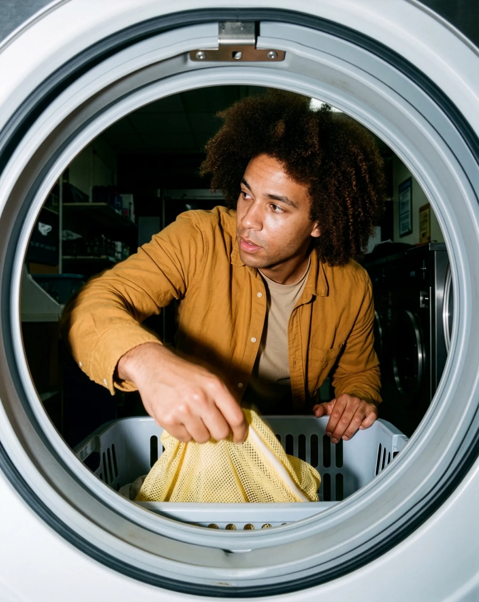 A man loading laundry, seen through the door of a washing machine