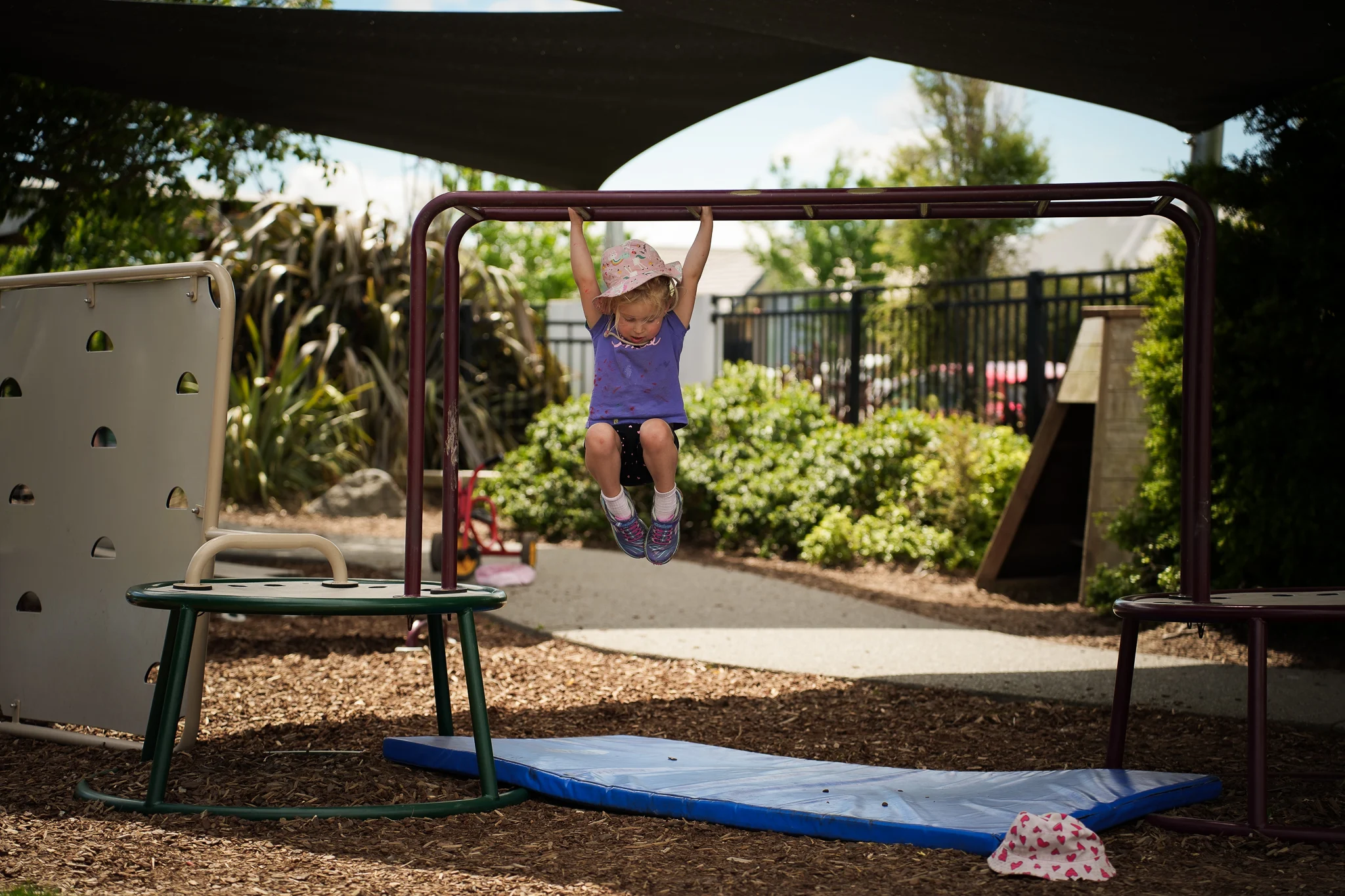 A child climbs and hangs from playground equipment in the outdoor play area.