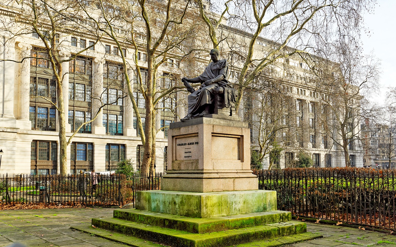 Estatua de bronce de Charles James Fox en el Jardín de la Plaza Bloomsbury, Londres, con el Museo Británico al fondo.
