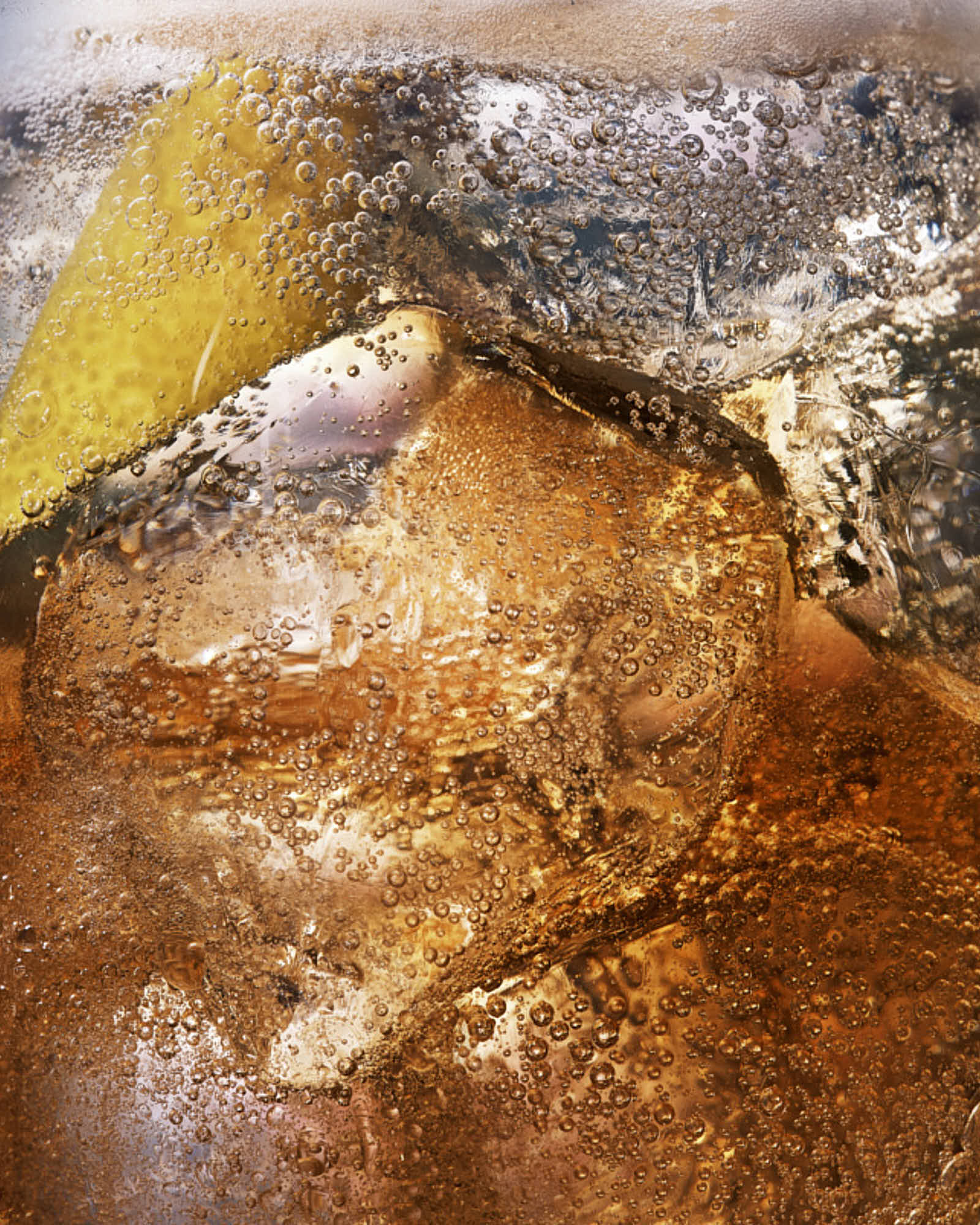 Close-up of ice cubes with shades of brown, gray, and yellow, showing fizzing and effervescence in a cocktail