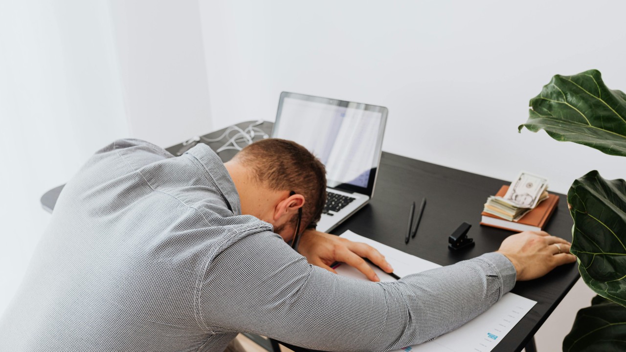 Male-presenting person tired and laying head down on their desk