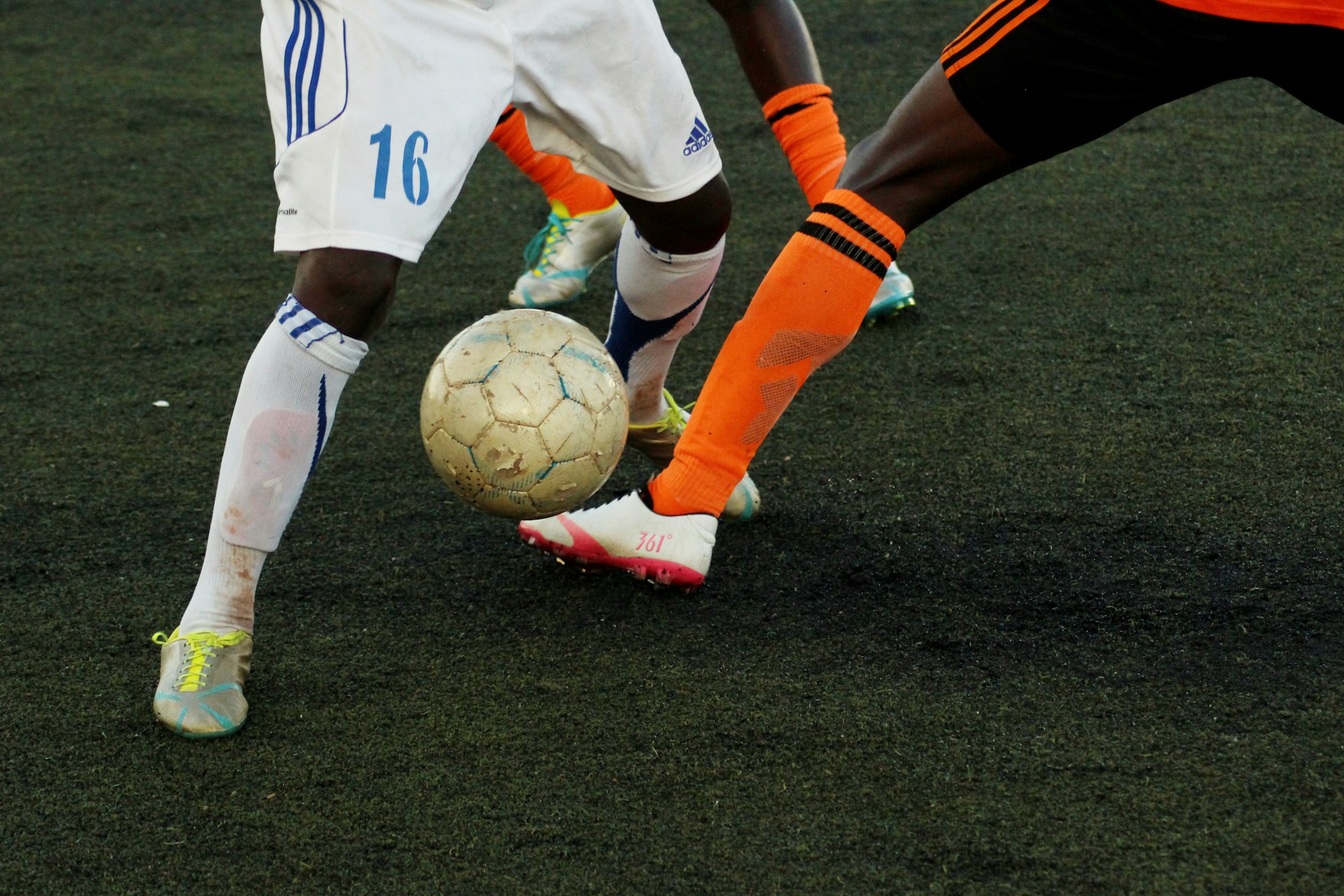 Close-up of soccer players' legs battling for the ball on artificial turf.