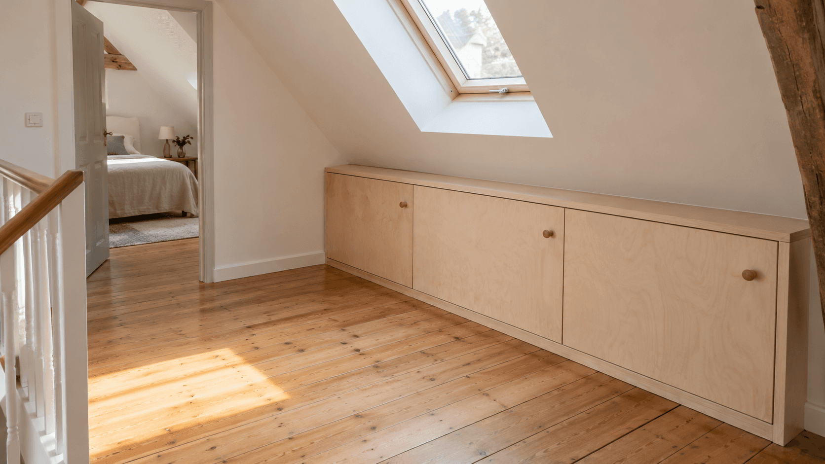 Placard bas en bois clair aménagé sous la pente d’un toit, devant un palier dégagé éclairé par une fenêtre de toit.