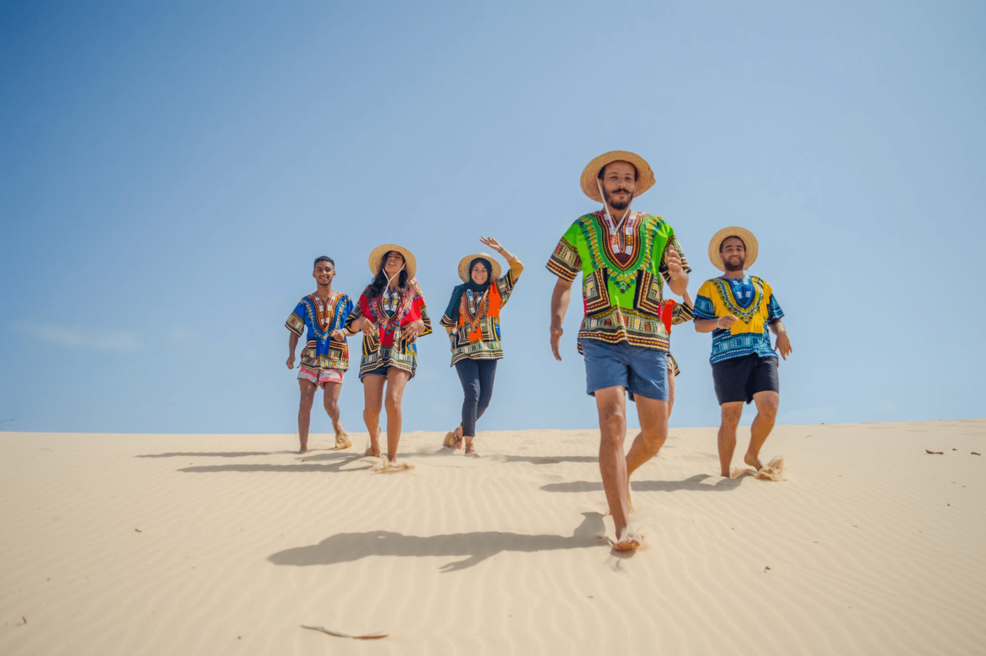 A group of children running playfully on a sandy beach under a clear blue sky.