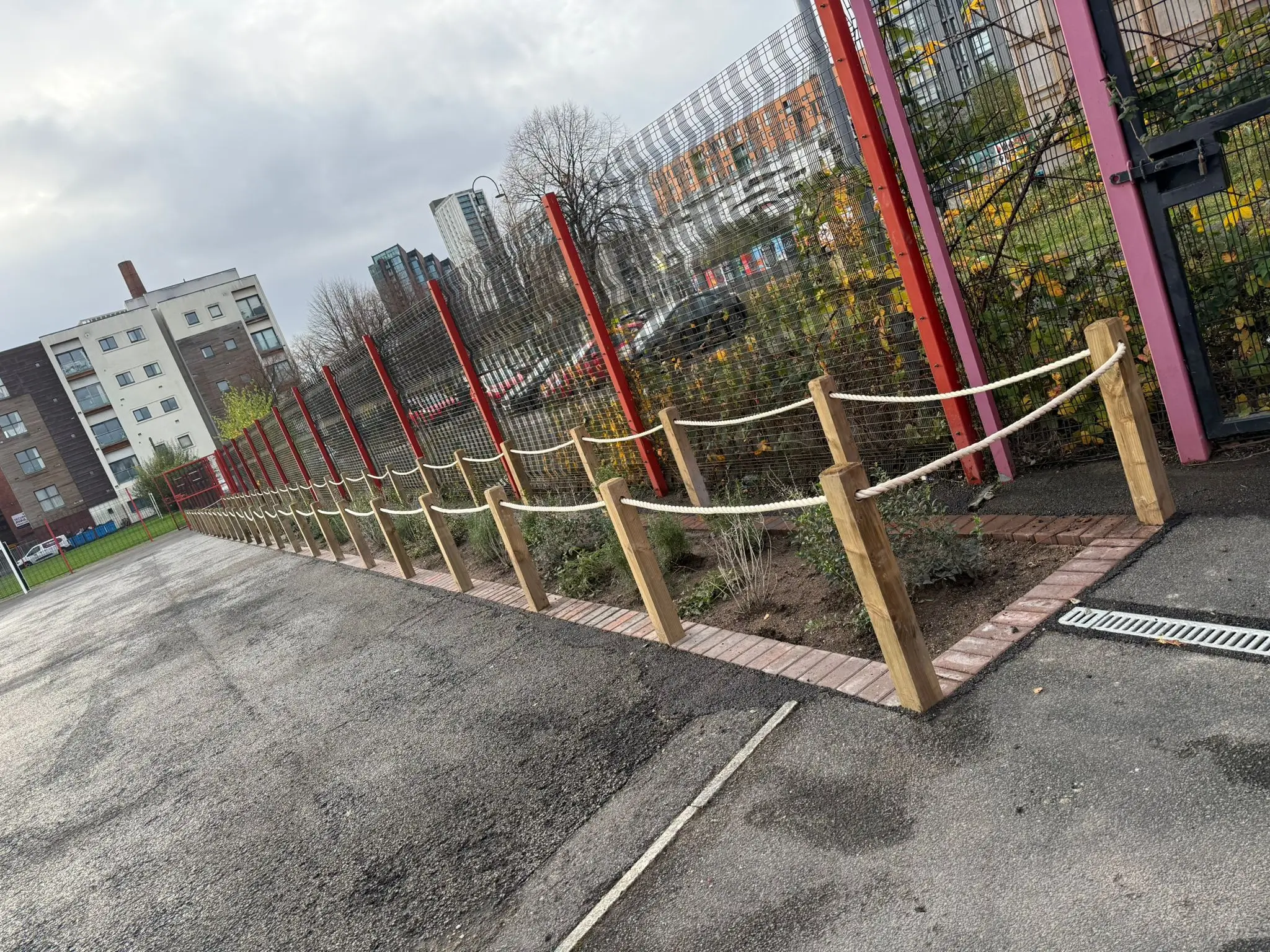 A wooden fence surrounds a garden area, with cloudy skies and buildings in the background.