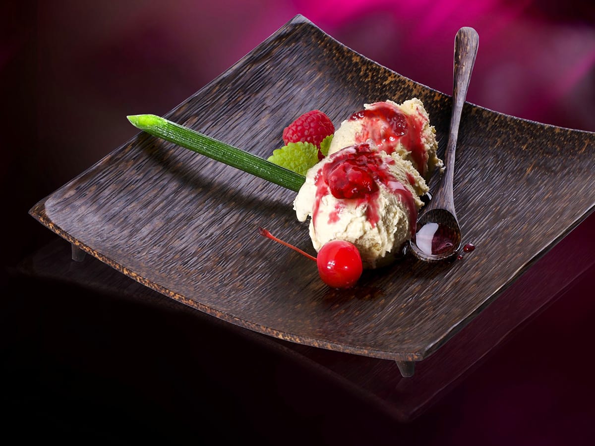 Vanilla ice cream with raspberry sauce, berries and cherry on dark plate, magenta backdrop