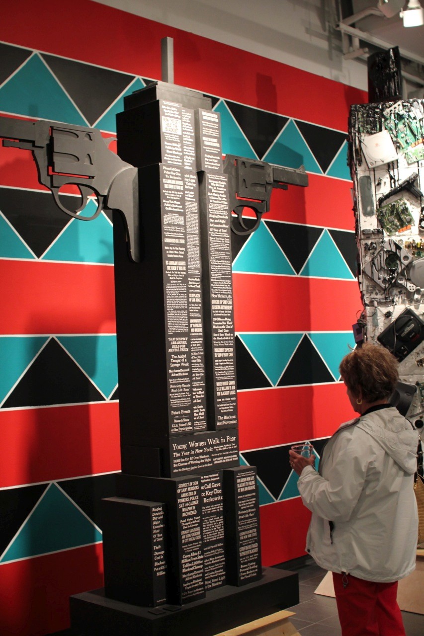 A photo of a totem structure that looks like a New York sky scraper, with white text and two barrel pistols sticking from it.
