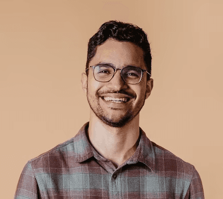 a young man wearing glasses standing in front of a mountain