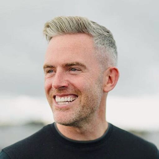 A woman with short curly hair wearing a black t-shirt looks into the camera.