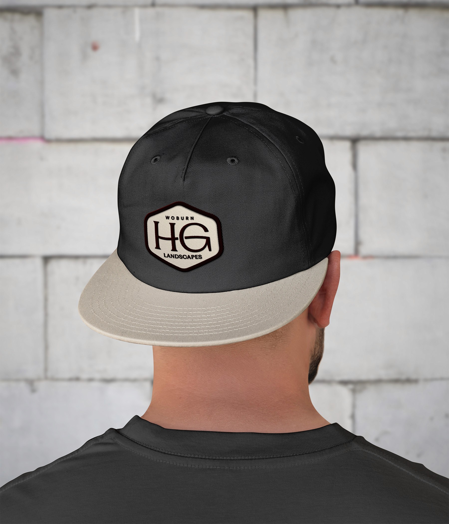 Person wearing a black and beige cap, viewed from the back, against a light gray brick wall.