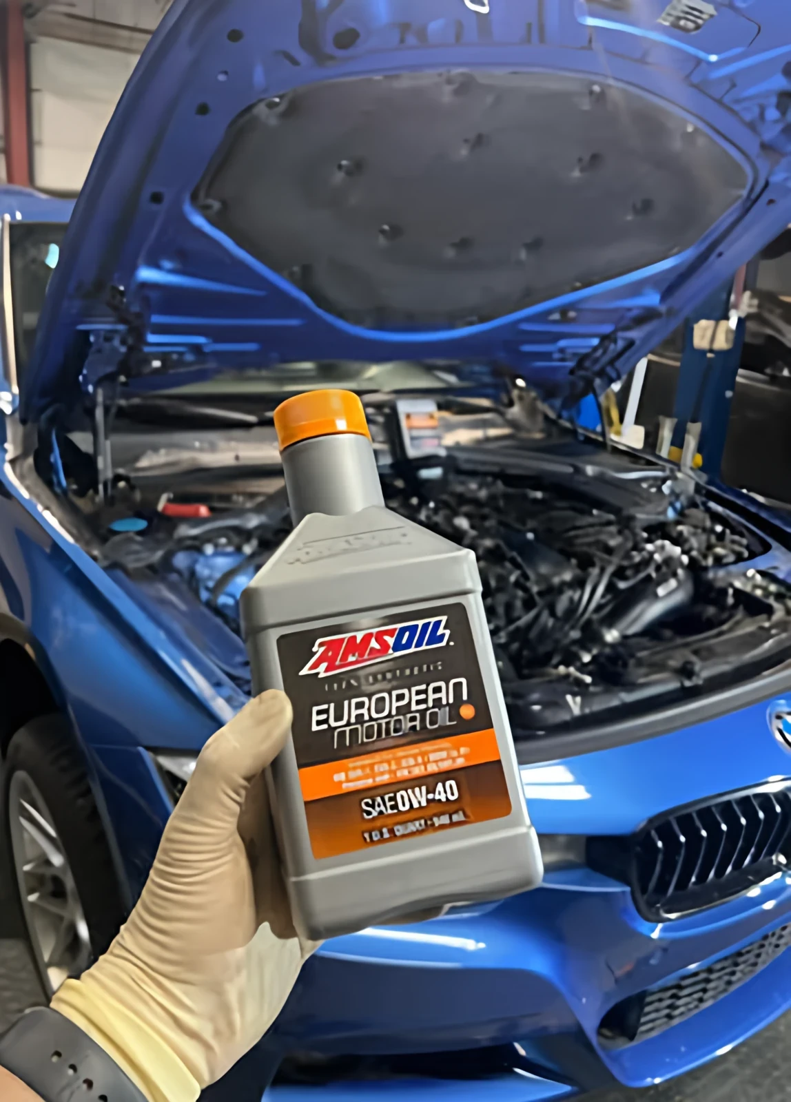 Gloved hand holding a bottle of motor oil in front of a blue BMW with its hood open
