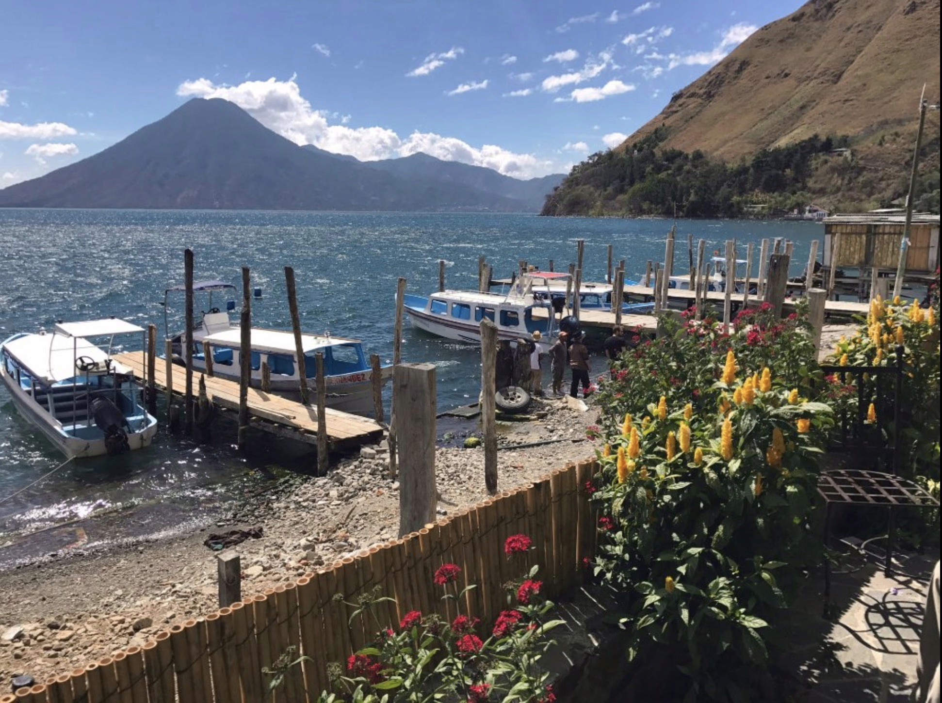 Wooden docks with several boats on a lake beside a flowering garden.