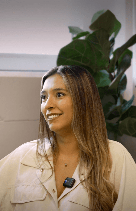 Smiling female therapist with short gray hair, wearing a brown top and a purple shawl, surrounded by a cozy background.