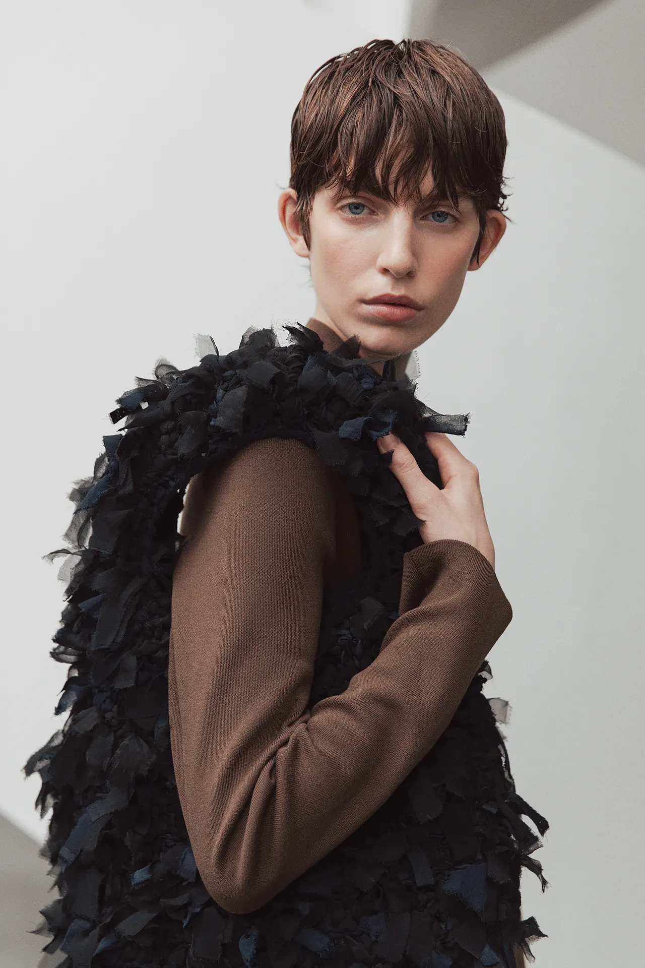 Aida Barni SS26 collection model wearing a brown knit outfit, carrying a large dark fringed and textured bag over her shoulder.
