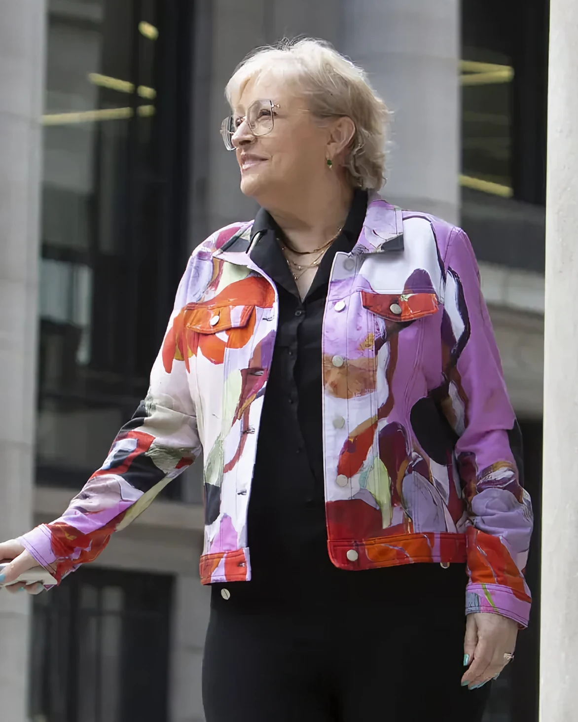 Christiane Constantineau, souriante, en veste à motifs colorés, appuyée à une rampe devant des colonnes de pierre