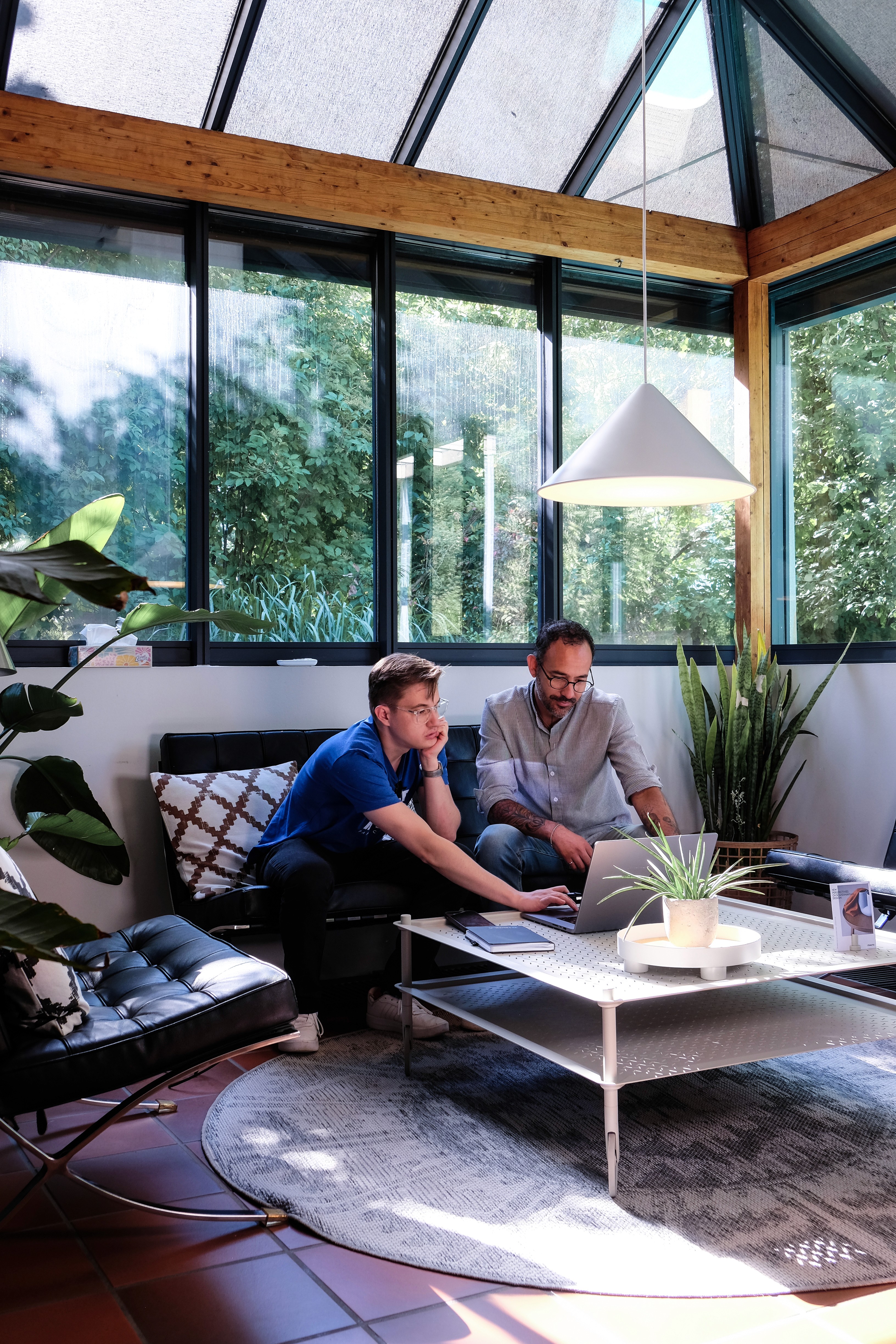 Zwei CONQUEST-Teammitglieder arbeiten gemeinsam am Laptop im Wintergarten des Büros Leonding — Strategiemeeting der B2B-Werbeagentur
