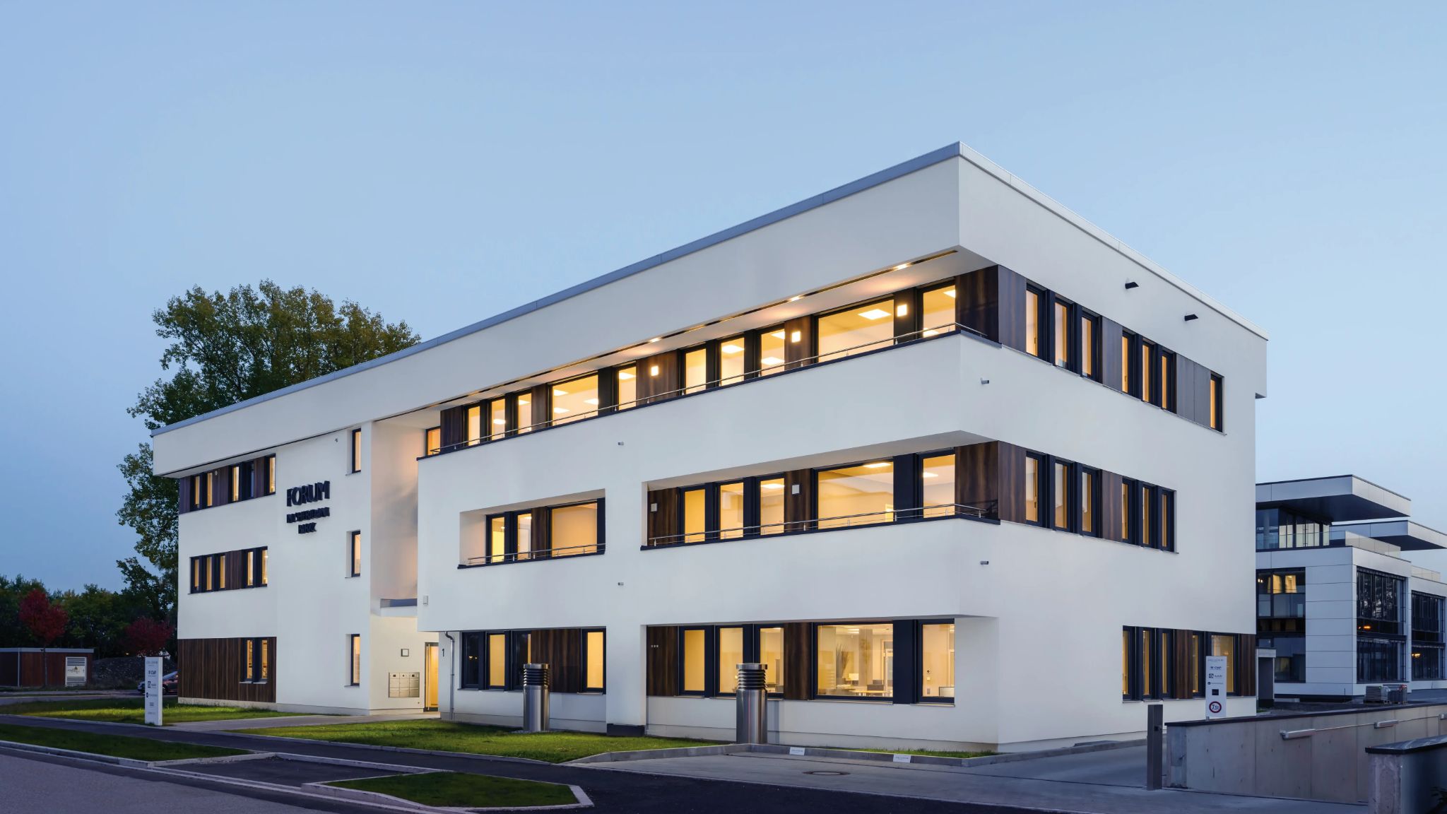 Blick auf modernes Bürogebäude mit Parkplatz davor.