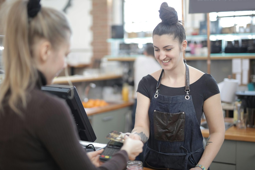 A visitor to Canada using a Canadian debit card to pay a smiling barista at a local coffee shop, illustrating how tourists can avoid foreign transaction fees by opening a local bank account.
