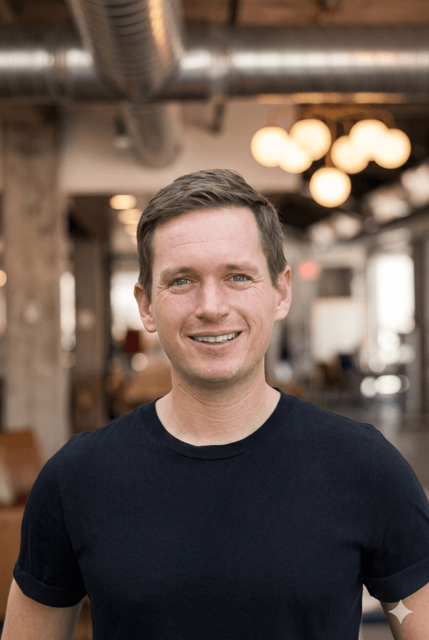 Mature man and a trimmed beard smiling confidently, standing in warm natural light against a modern backdrop.