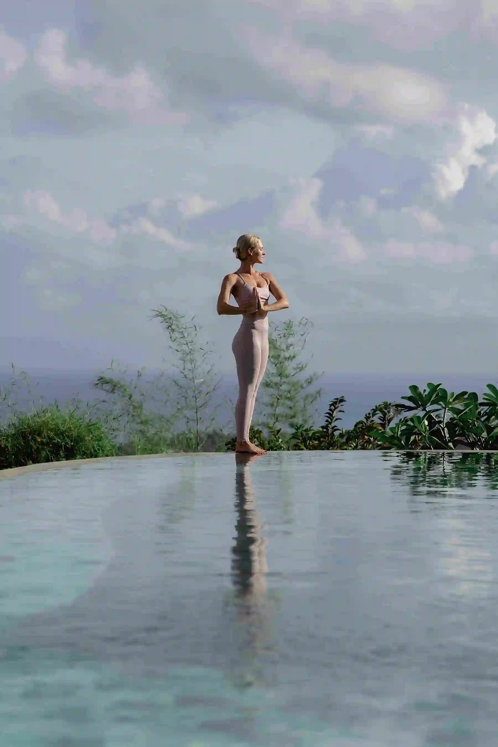 Yoga student standing in prayer pose by the infinity pool overlooking the ocean at Ulu Yoga Bali resort.