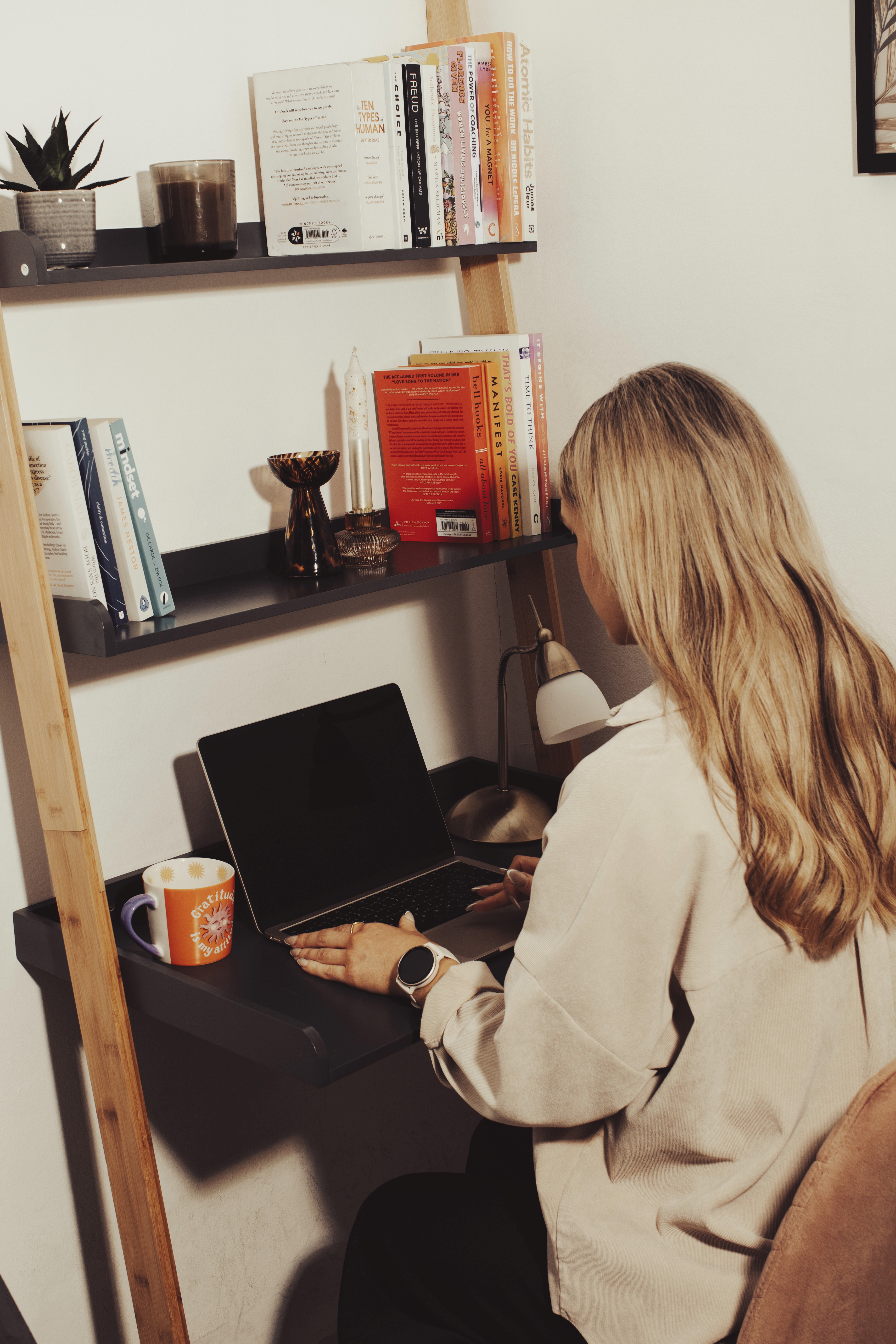 Person sitting at a table using a laptop, holding glasses, in a bright, relaxed home setting.