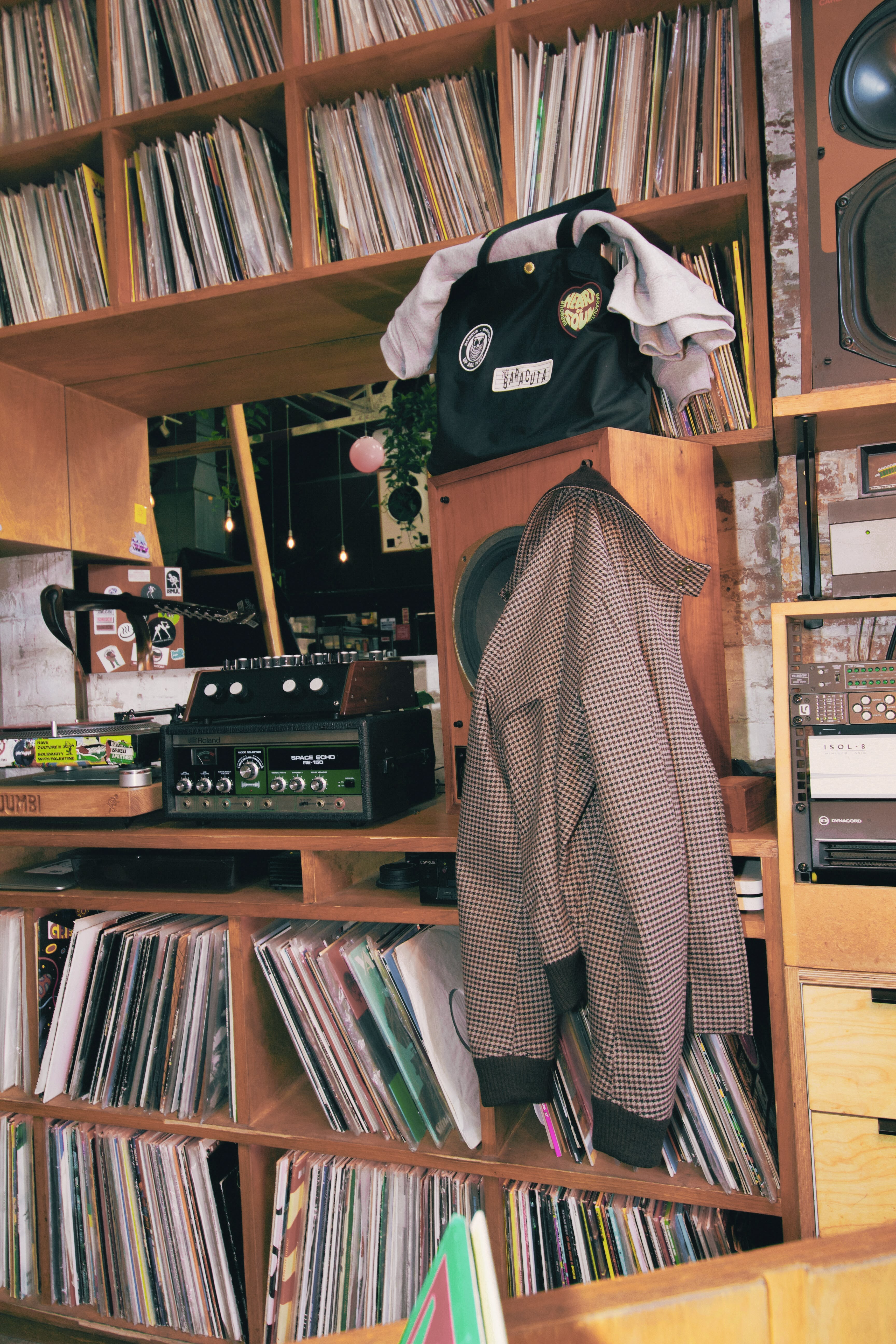 Dans une installation de disc-joker avec platines et étagères pleines de disque vinyl, un blouson à carreaux issu de la collab Barbour x Baracuta est accroché