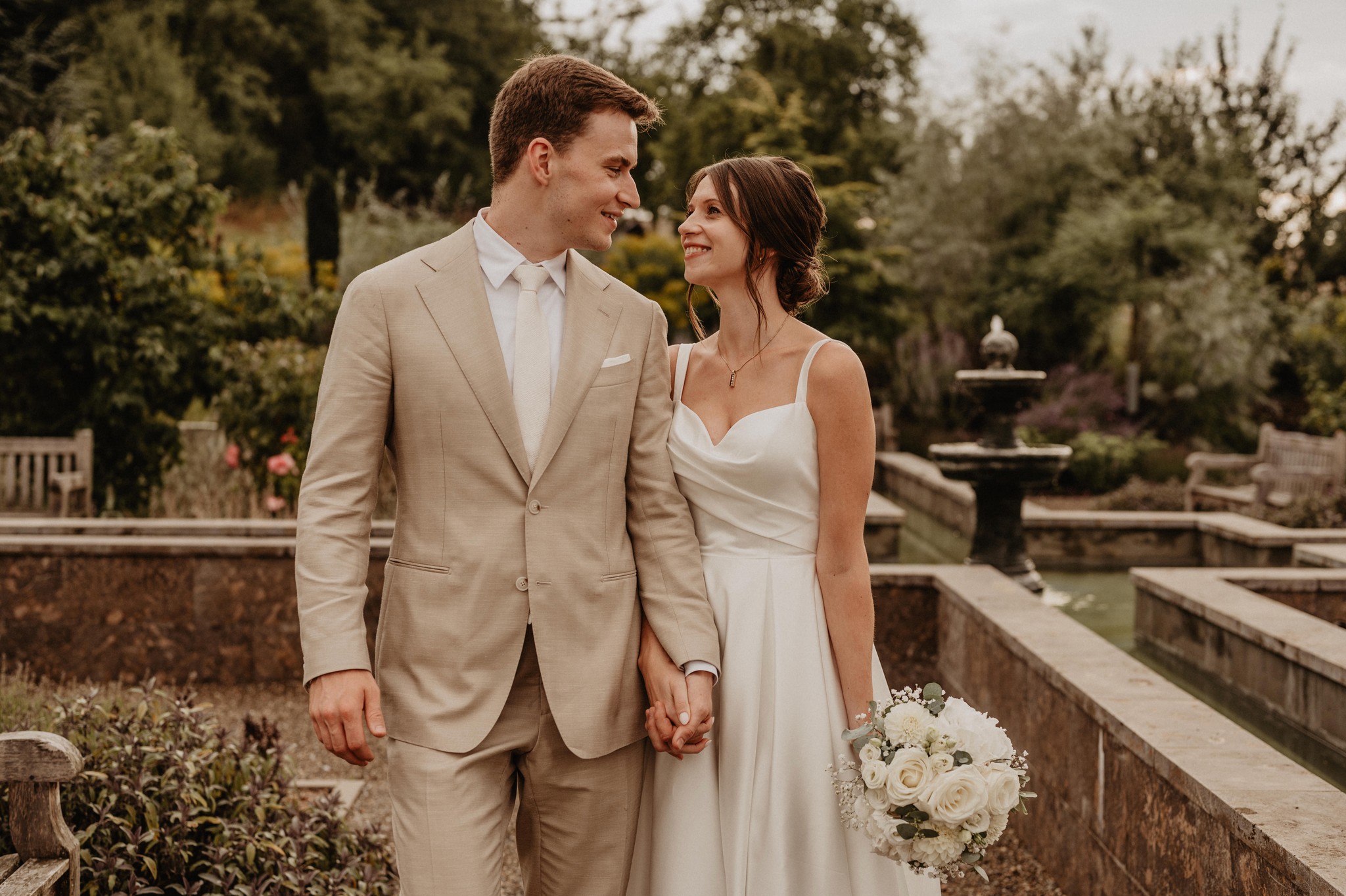 Ein Brautpaar hält Händchen in einer romantischen Gartenanlage – gefühlvolle Hochzeitsfotografie von Nicole Grasmann aus der Nähe von Würzburg