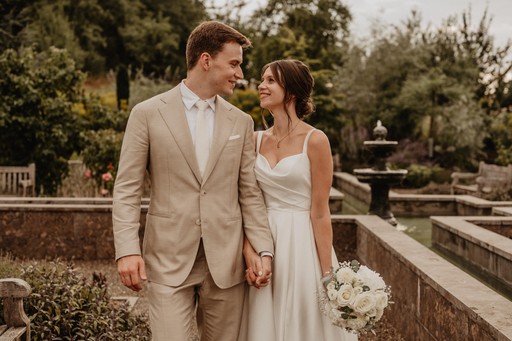 Ein Brautpaar hält Händchen in einer romantischen Gartenanlage – gefühlvolle Hochzeitsfotografie von Nicole Grasmann aus der Nähe von Würzburg