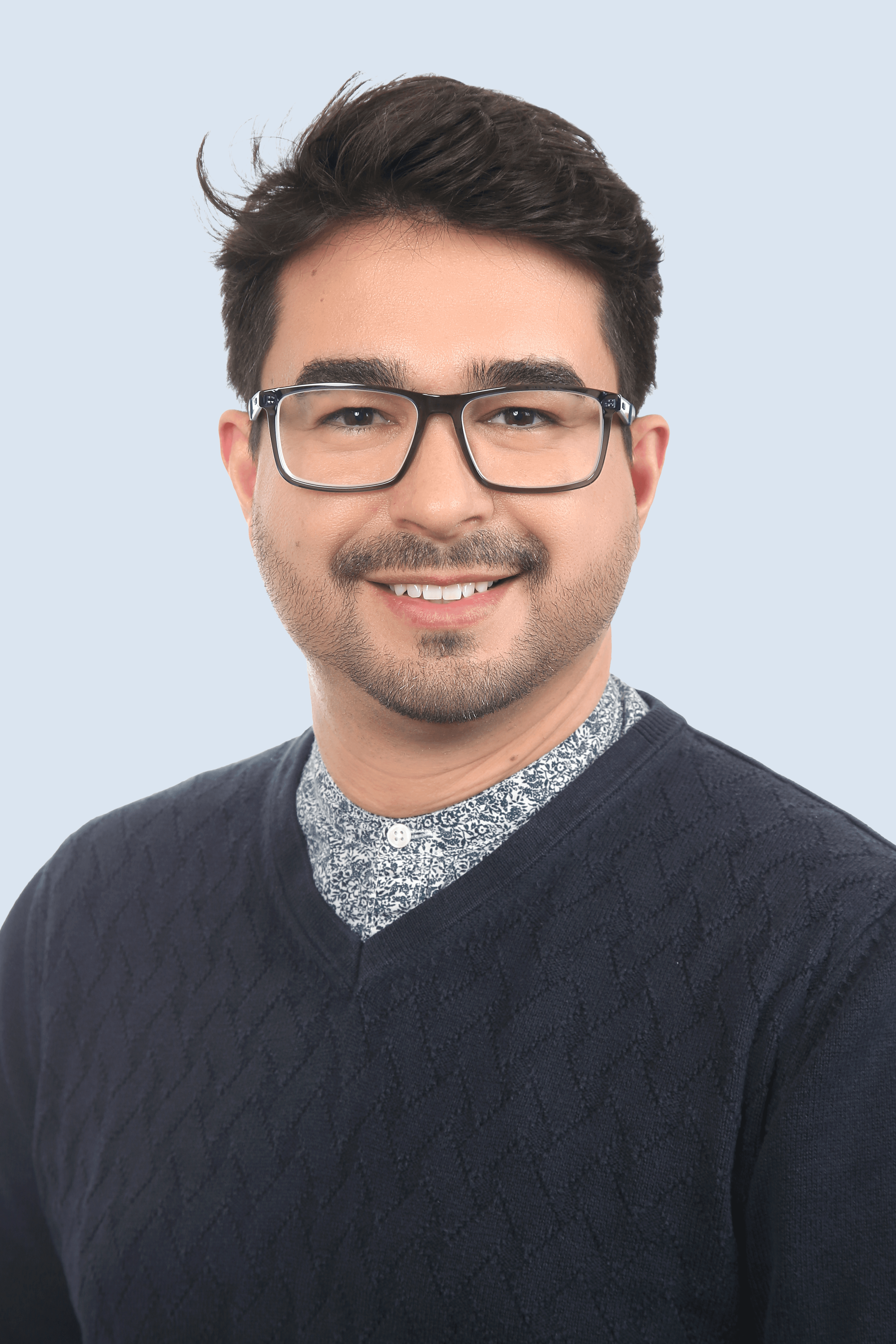 Frau mit braunem Anzug, blauem Hemd und Brille schaut mit verschränkten Armen seitlich in die Kamera und lächelt.