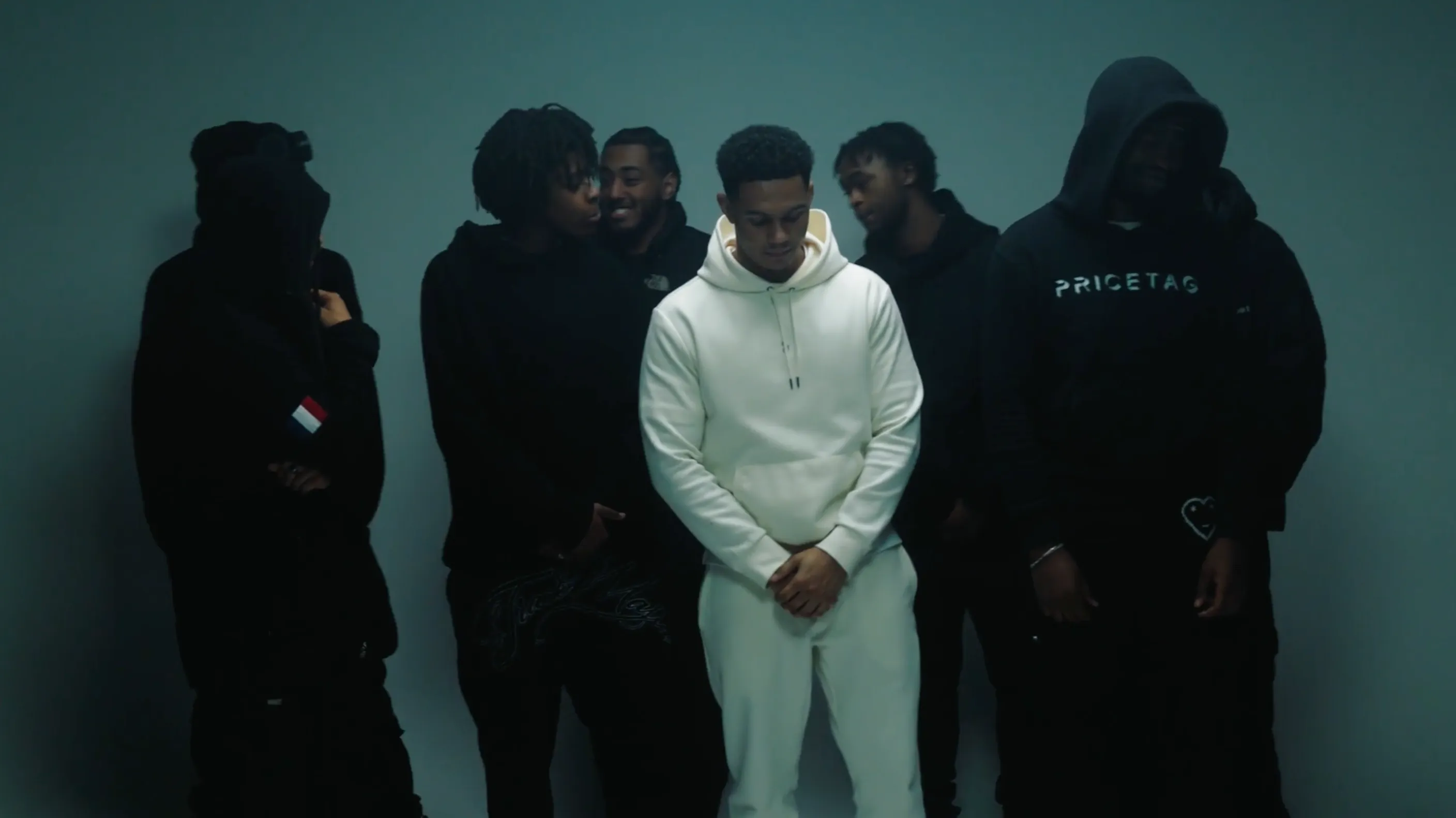 A group of men in black tracksuits with a man in a white tracksuit in the middle