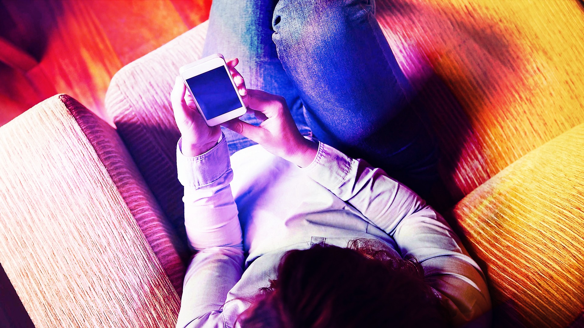 A woman sits on a couch, looking at her phone