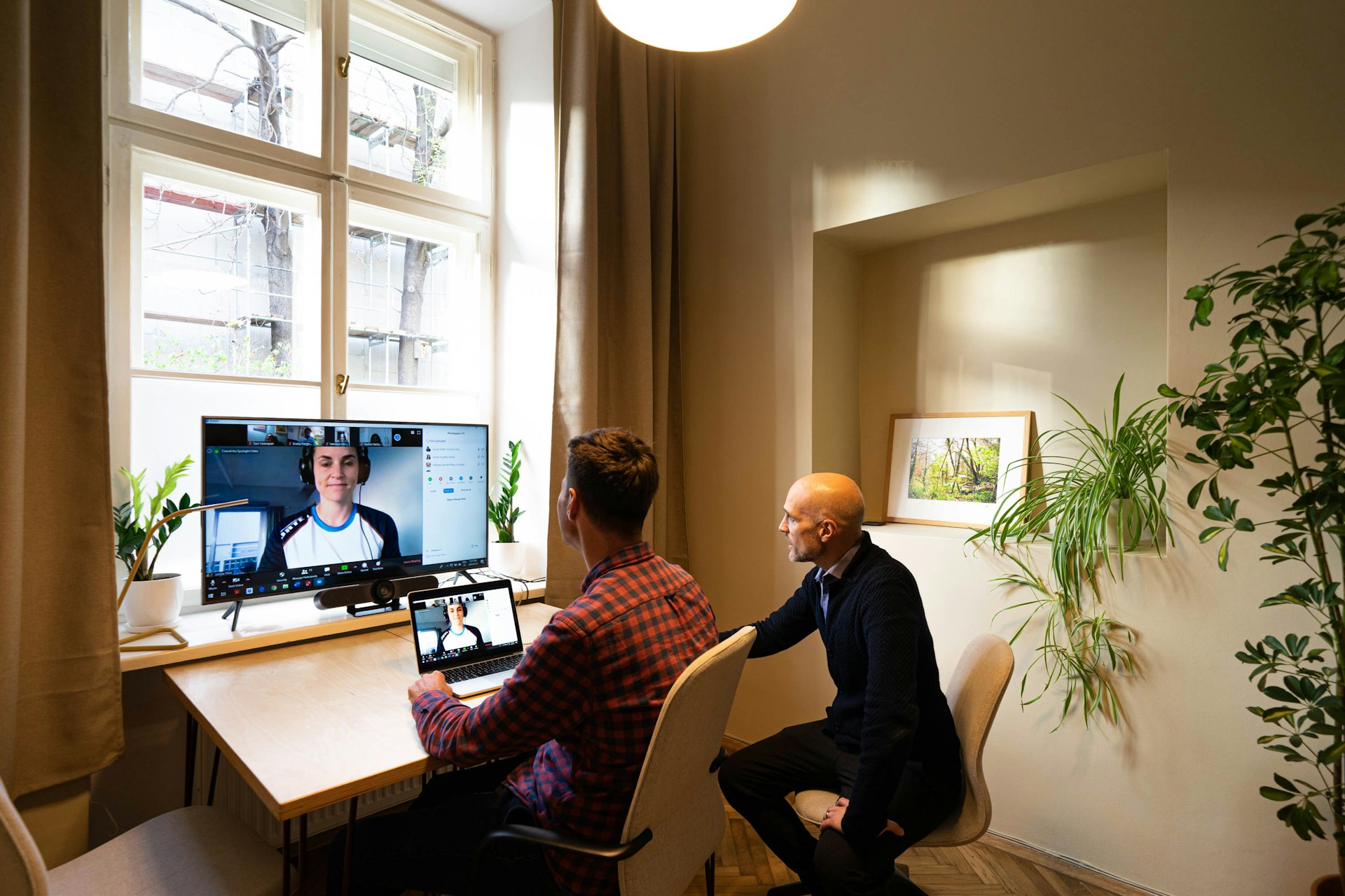 tow men sitting at an office on a video call with someone on the screen in a mentoring call