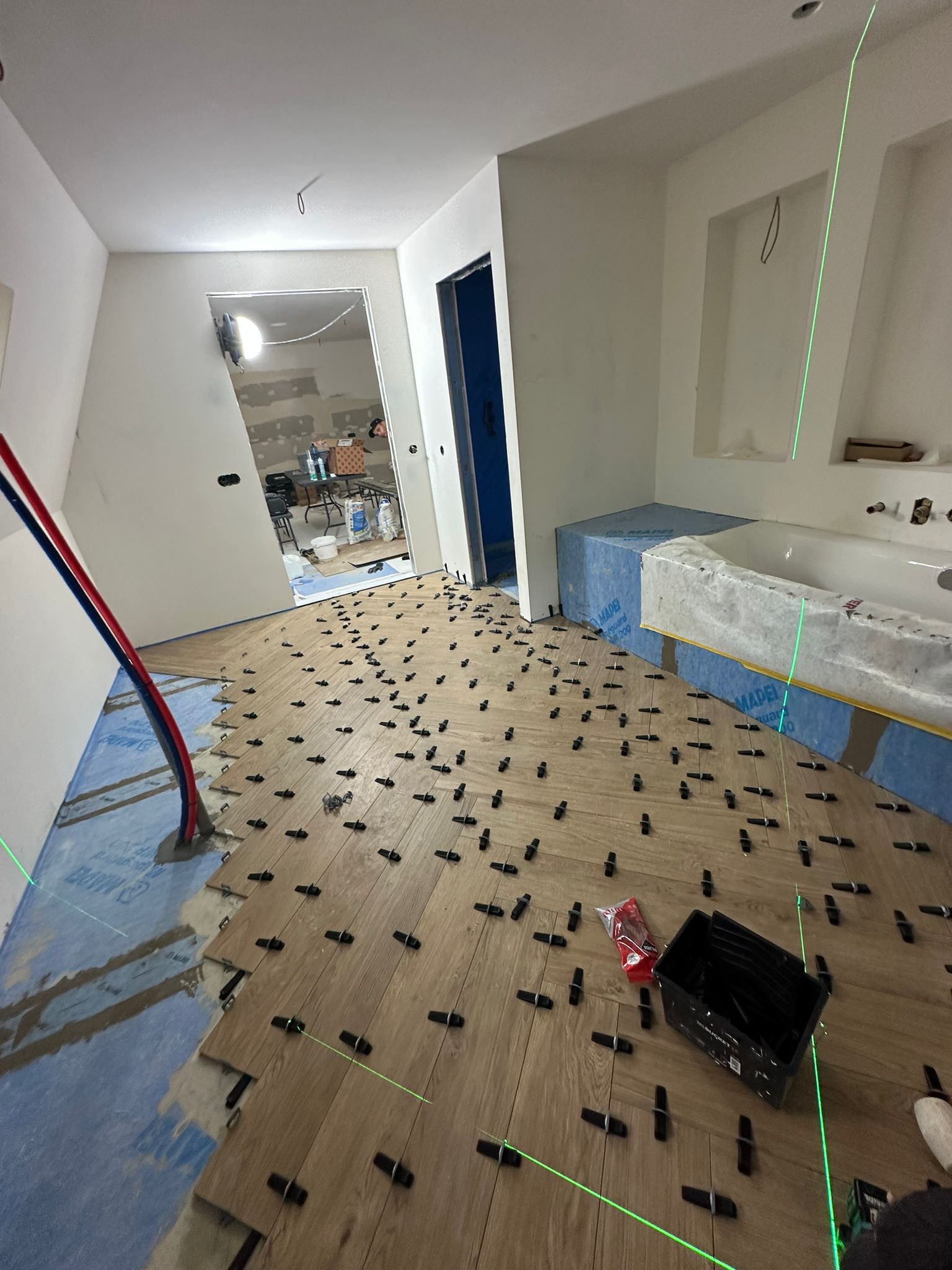 Spacious modern apartment with a kitchen island, black chairs, and stainless steel appliances. A cozy living area with armchairs and plants in the background.