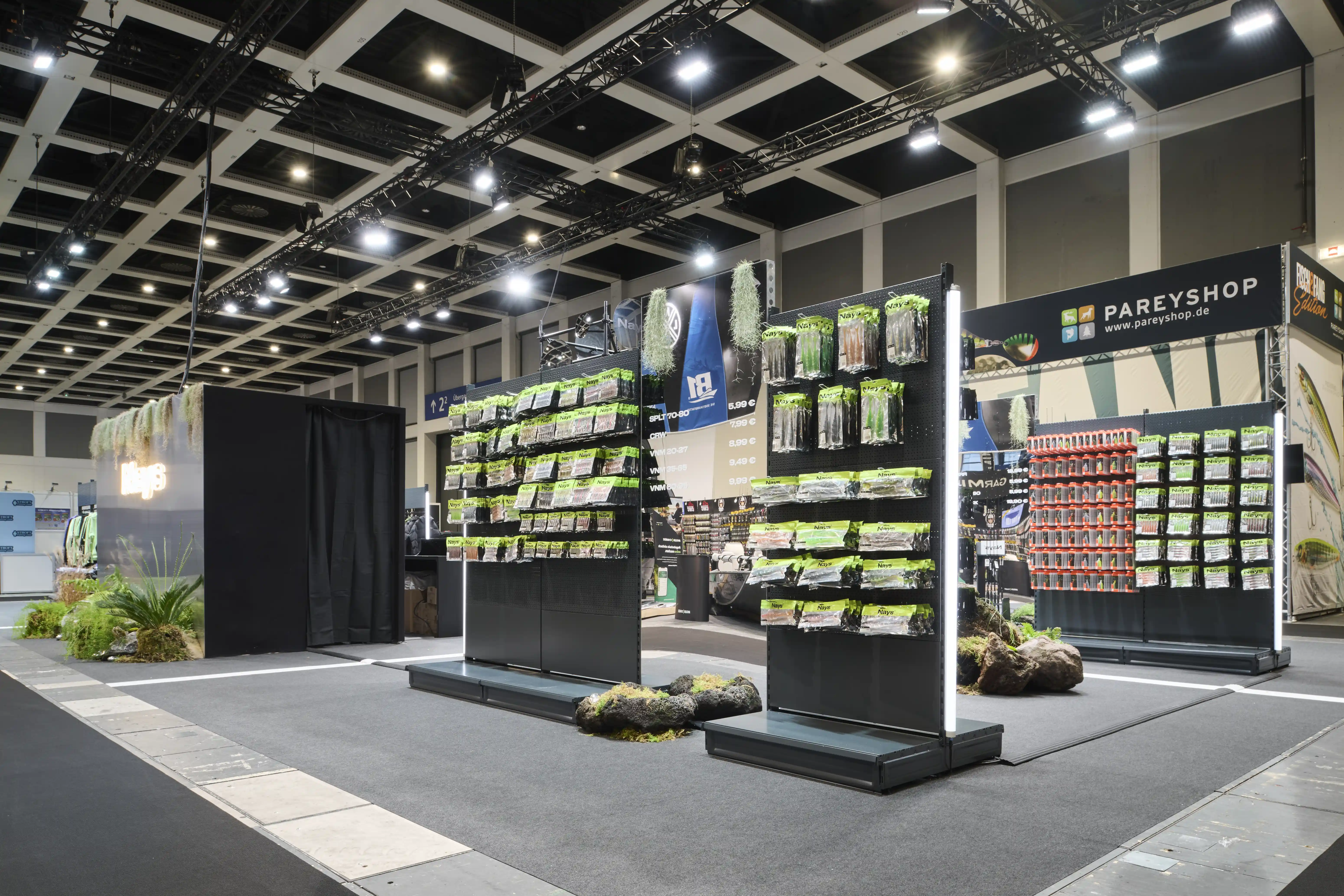 Overview of the Nays booth with black product gondolas full of lure packaging and rock islands on grey carpet.