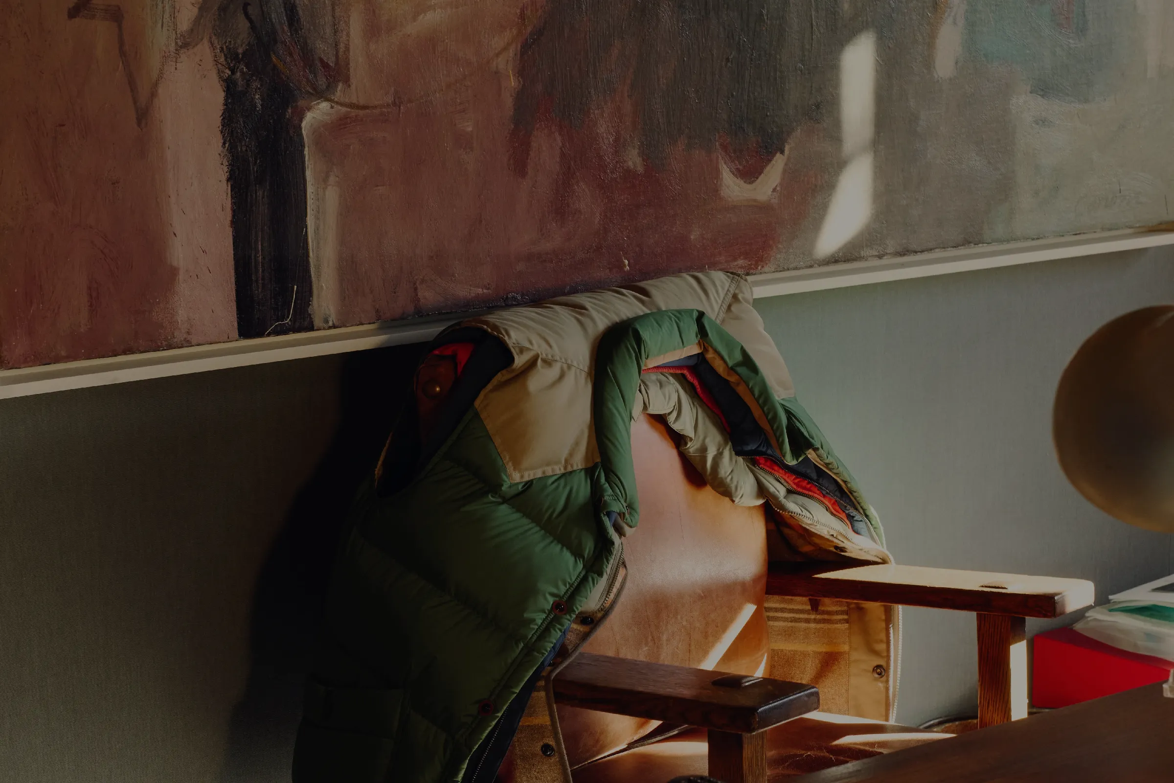 Green jacket draped over a wooden chair beneath a large abstract painting.