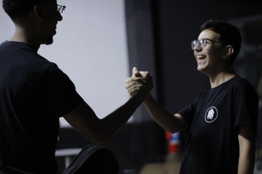 A group of four people standing outside a building, engaging in conversation, with cars parked nearby.