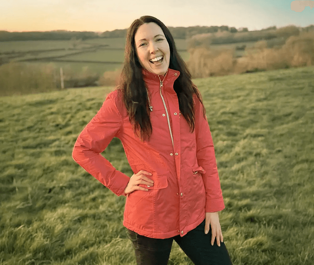 Smiling woman in beige linen outfit standing indoors with plants and books in the background.