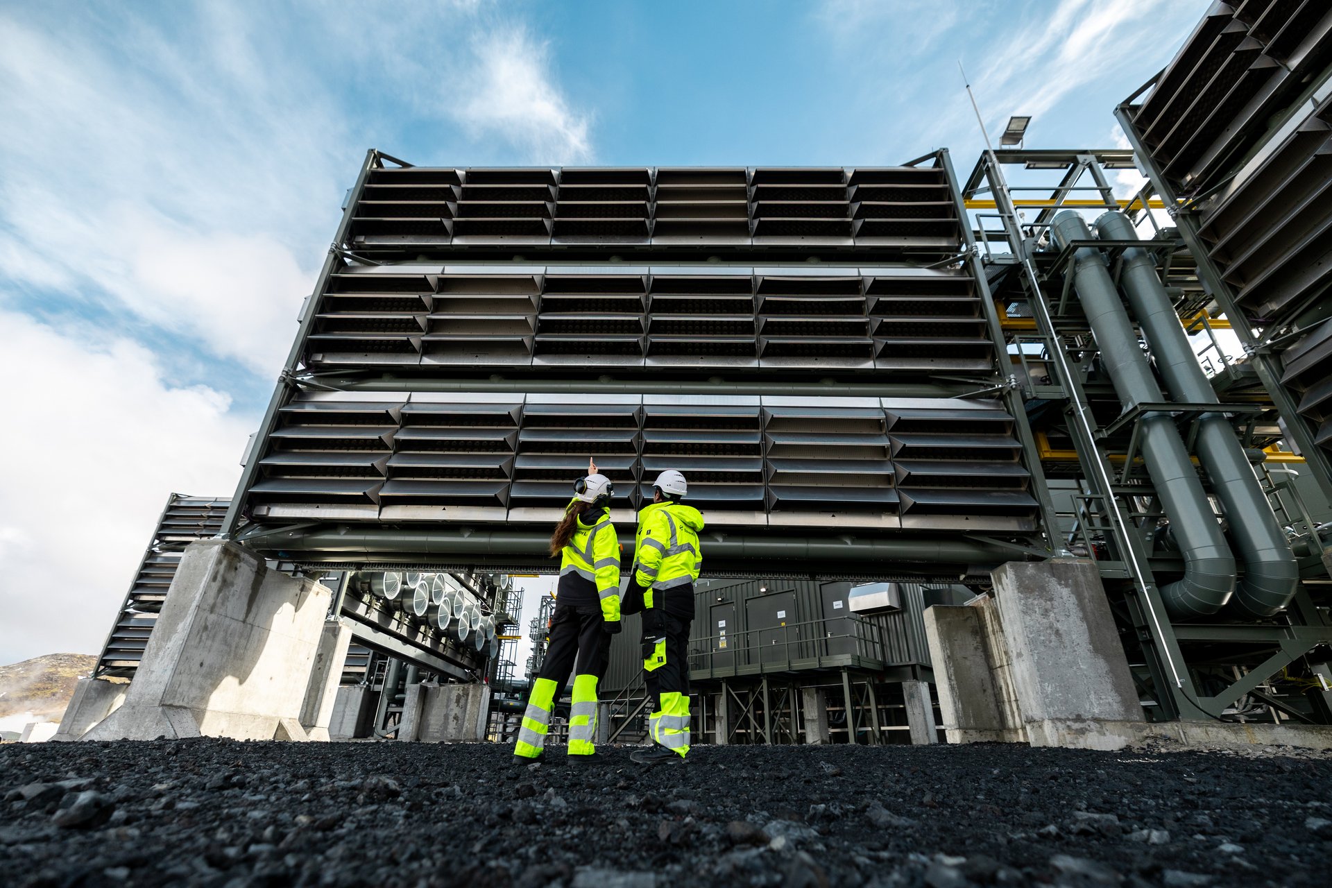 Two engineers in high-visibility gear stand in front of Climeworks’ Mammoth direct air capture (DAC) facility in Iceland, the world’s largest carbon removal plant designed to capture and store up to 36,000 tons of CO₂ annually by injecting it into basalt for permanent mineralization. Photo: Climeworks