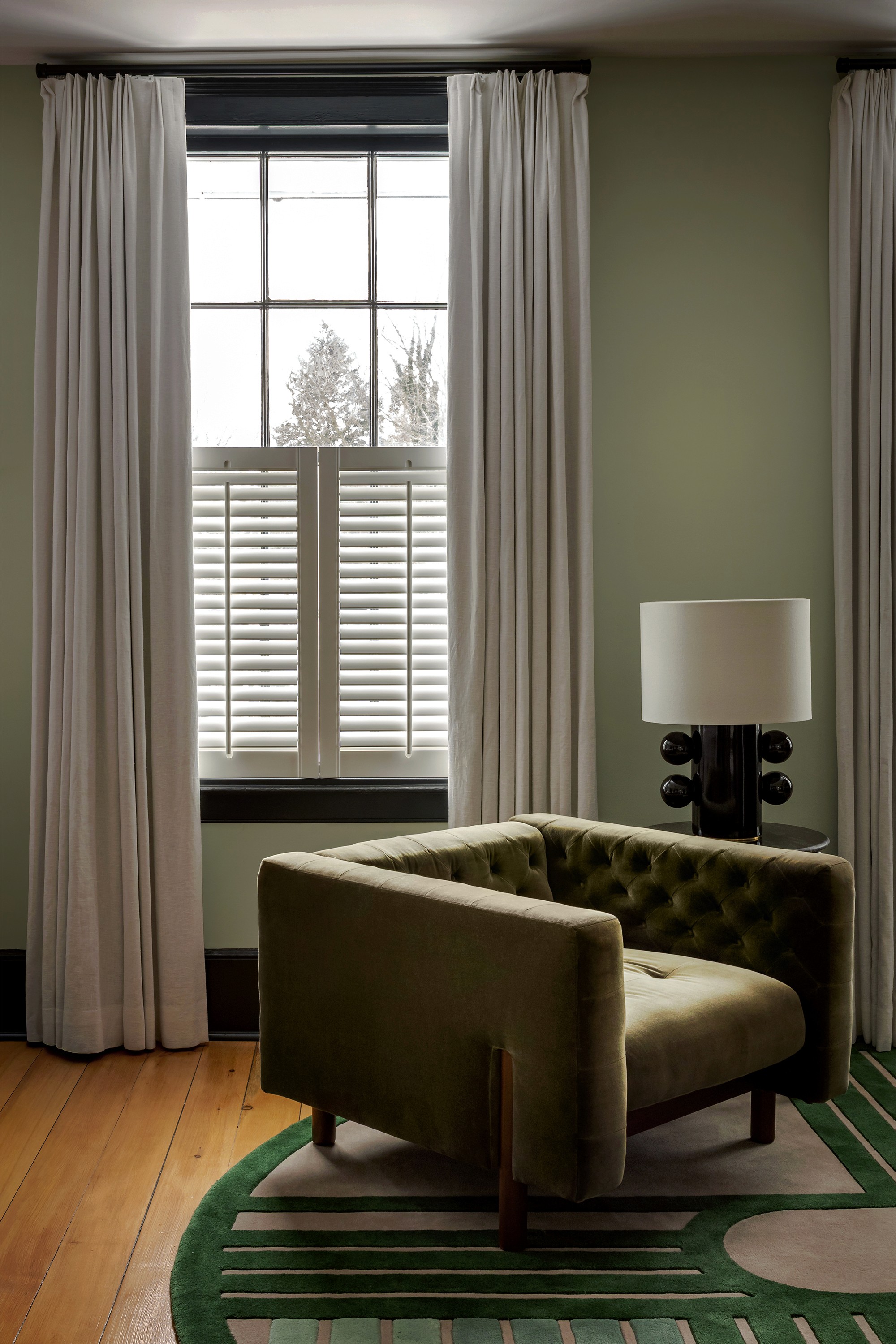 Hattan House principal bedroom lounge area, green velvet armchair and Kelly Wearstler Tiglia table lamp on custom New Zealand wool rug beside plantation shutters