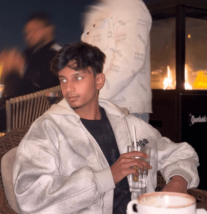 A person with blond hair wears a dark coat and a beige turtleneck sweater. They have a calm expression, against a neutral background.