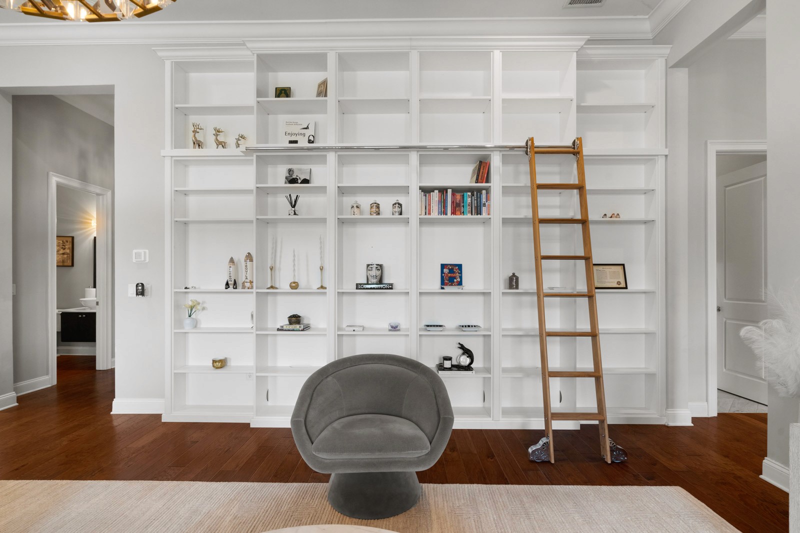 Living room wall of white built-in shelves with a rolling library ladder and a gray swivel chair, in a Beach Park home