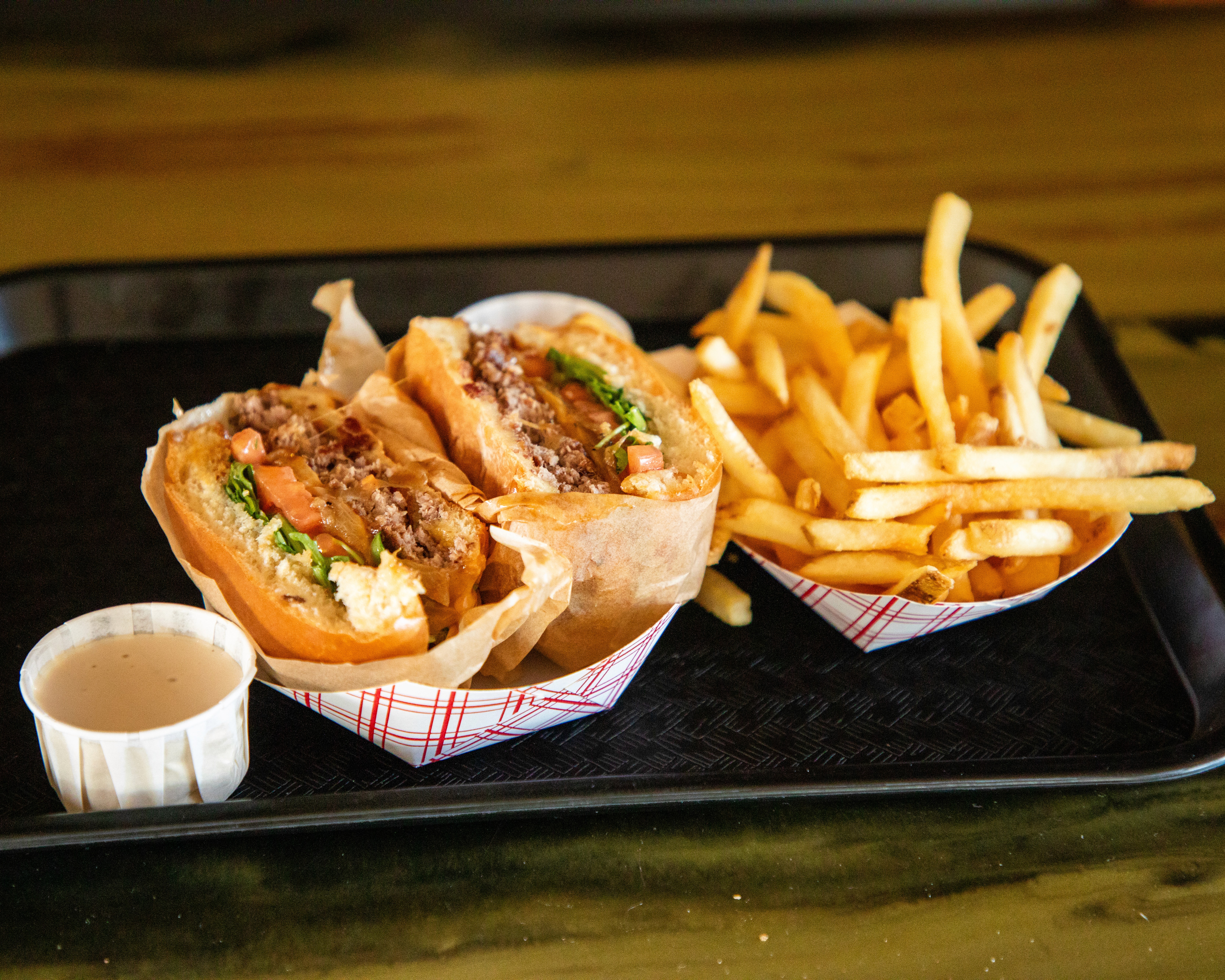 An overhead shot of a large oval plate featuring sliced, roasted duck, half glazed with a sauce, served over two thin pancakes and alongside steamed bok choy, surrounded by small bowls of condiments like scallions, sauce, salt, and carrot shreds.
