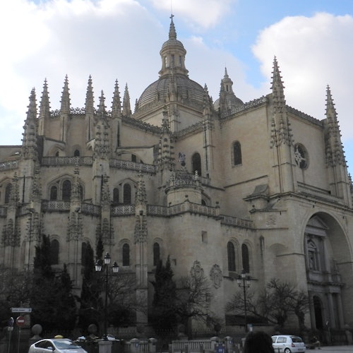 A large, ornate Gothic cathedral with pointed spires, arched windows, and a central dome under a partly cloudy sky.