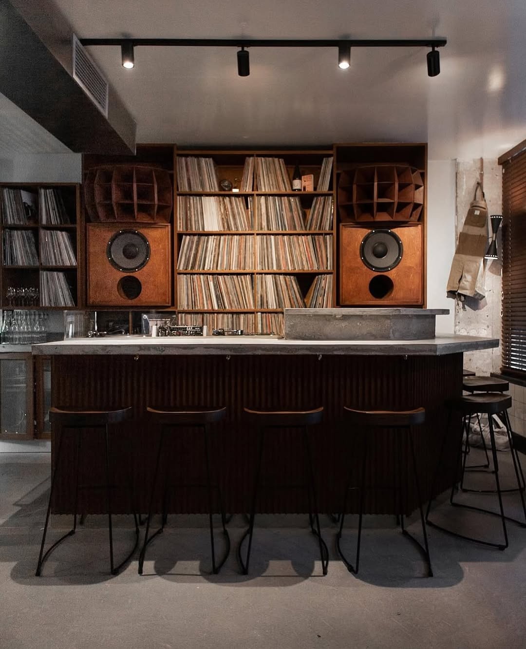 Moody interior with illuminated record shelves, wine bottles, glassware, and a small lamp.