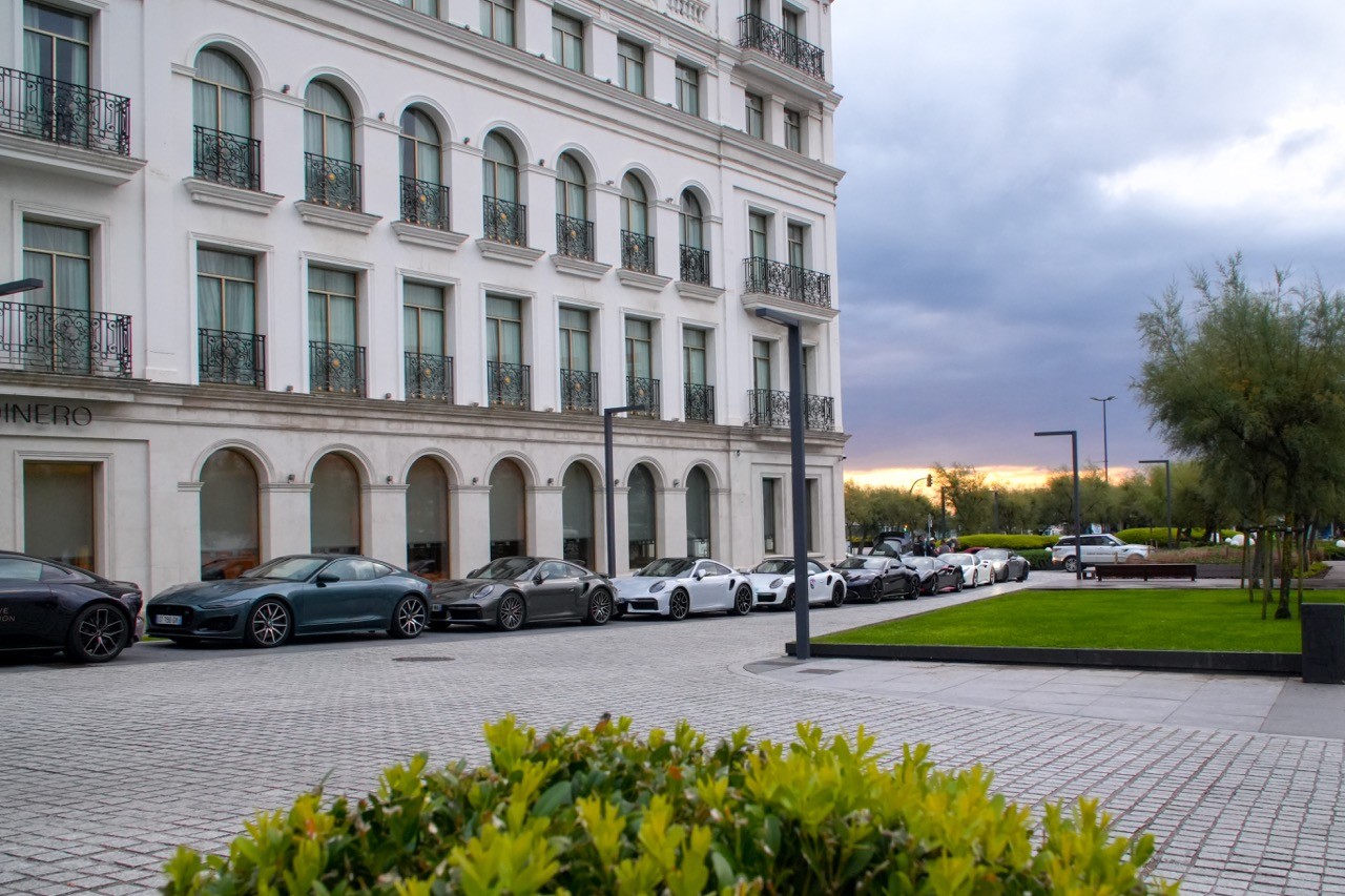 Voitures de sport garées devant un grand hôtel blanc au coucher du soleil, road trip Pics d’Europe