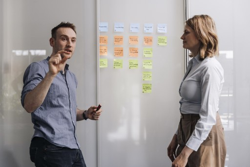 Jeremias Kuge und Diana Löffler bei Fünfpunktnull stehen vor einer Glastür mit farbigen Post‐its und diskutieren Strategien zur Customer Experience
