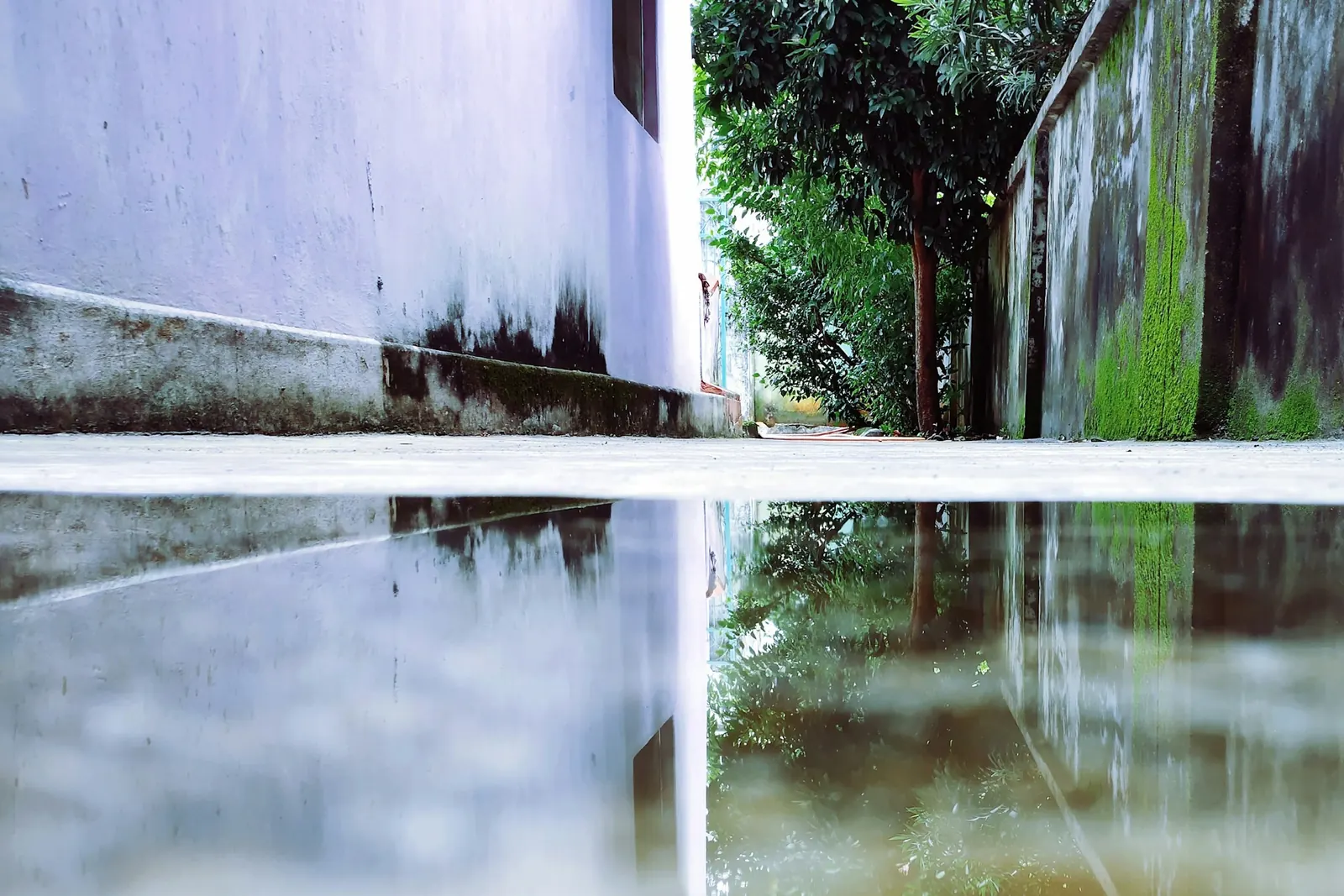 Light reflected in wet paving beside a plain wall after rain.