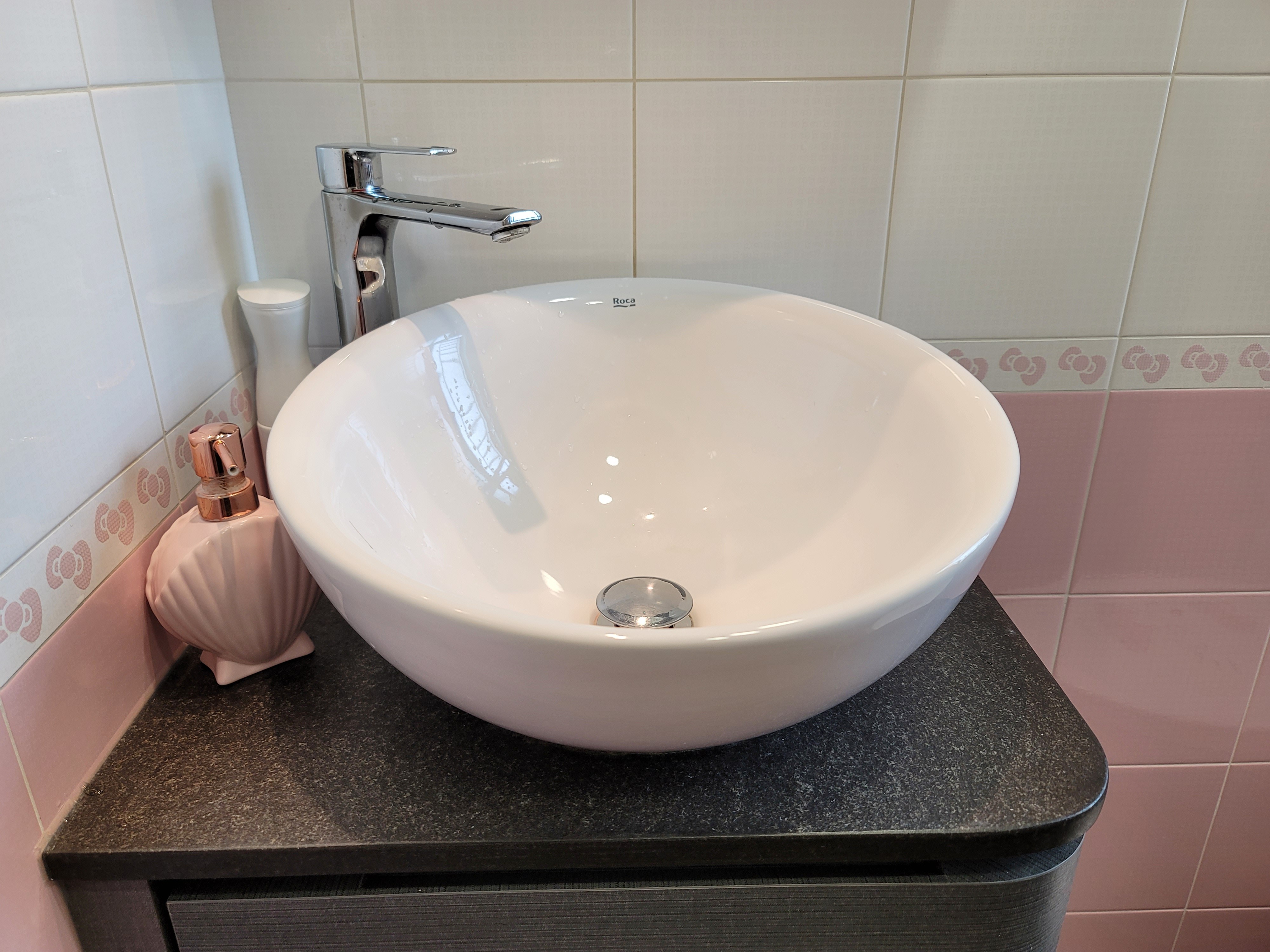 Polished chrome faucet over a white circular vessel sink mounted on a matte black countertop in Hoi Tat Estate.